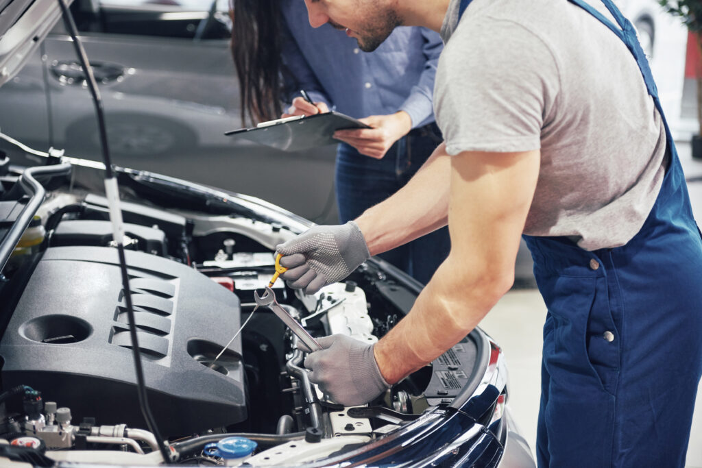 A man mechanic and woman customer look at the car hood and discuss repairs.